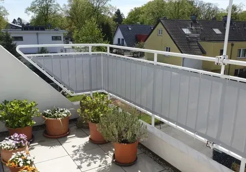 Balkongeländer mit grauer blickdichter Bespannung, davor Pflanzkübel, dahinter der Blick auf umliegende Wohnhäuser