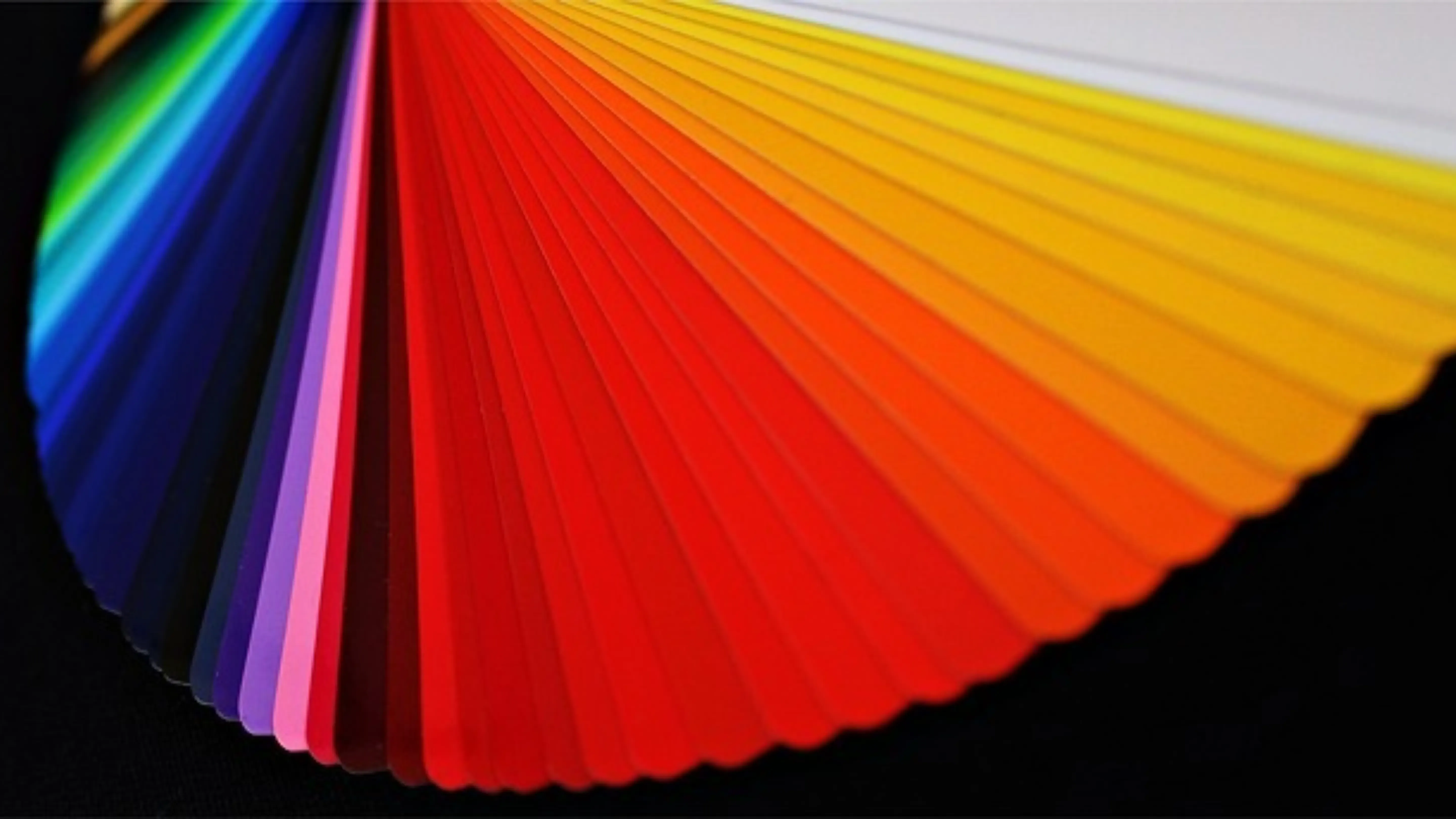 Aufgefächerter Farbfächer mit Musterkarten in Rot-, Orange-, Gelb-, Grün-, Blau- und Violetttönen vor dunklem Untergrund